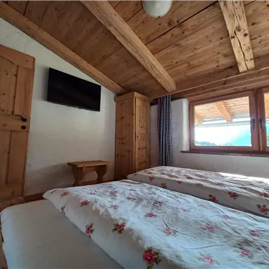 A cozy bedroom with two beds and wooden furniture. Large windows let in plenty of daylight.