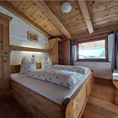 A cozy room with wooden ceilings and furniture. Two beds with white pillows and a view of nature.