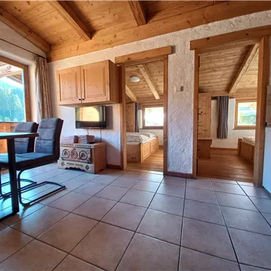 A cozy interior with wooden furniture and a dining table. The windows provide a view of the natural surroundings.