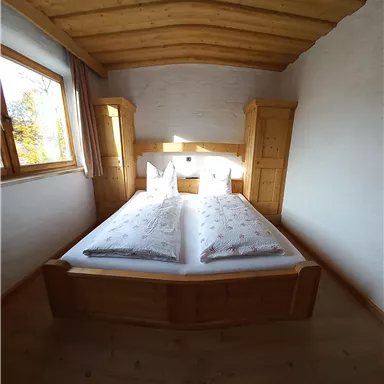 A cozy bedroom with a large bed and wooden cabinets. Light walls and a window create a pleasant atmosphere.