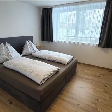 A modern bedroom with a double bed and two pillows. Large windows let in plenty of natural light.