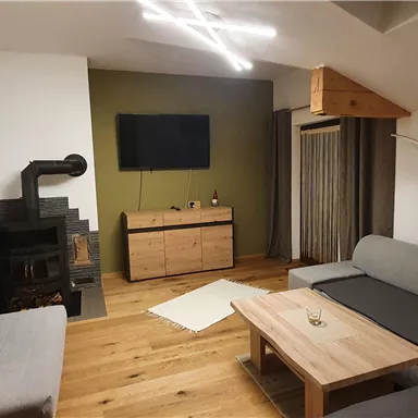 Ein modernes Wohnzimmer mit Holzfußboden und einer gemütlichen Couch. An der Wand hängt ein Bild von einer grünen Landschaft, und ein Ofen steht im Raum.