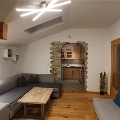 Ein modernes Wohnzimmer mit einer hellen Deckenlampe und stilvollen Möbeln. Der Raum hat Holzfußboden und eine große Fensterfront, die für eine angenehme Atmosphäre sorgt.