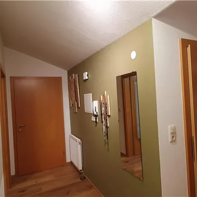 Ein heller Flur mit einer grünen Wand und Holzboden. An der Wand hängen Bilder und es gibt mehrere Türen.