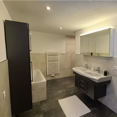A modern bathroom with a bathtub, a large vanity sink, and a towel radiator. The walls are in neutral tones, and the lighting is bright and inviting.