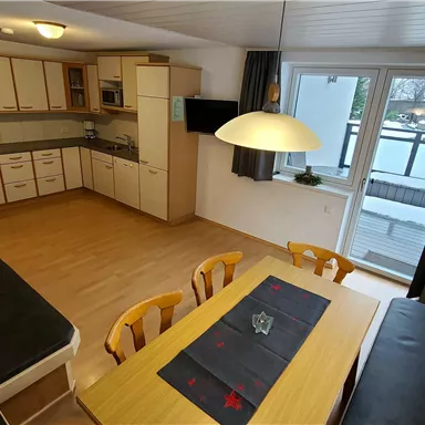 A modern kitchen with a large dining table and cozy chairs. Large windows ensure plenty of daylight.