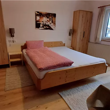 Ein gemütliches Schlafzimmer mit einem großen Bett und Holzmöbeln. Ein Fenster bietet einen Blick nach draußen und ein kleiner Tisch steht im Raum.