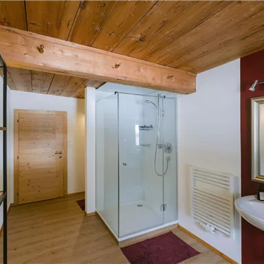 Ein modernes Badezimmer mit einer Glasdusche und einem Waschbecken. Der Holzdecke und die rote Wand schaffen eine gemütliche Atmosphäre.