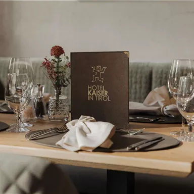 An elegant table in the restaurant with glass wine glasses and beautifully folded napkins. On the table lies the menu of the Hotel Kaiser in Tyrol.