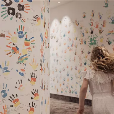 A girl is walking through a room with colorful handprints on the walls. The atmosphere is lively and creative.