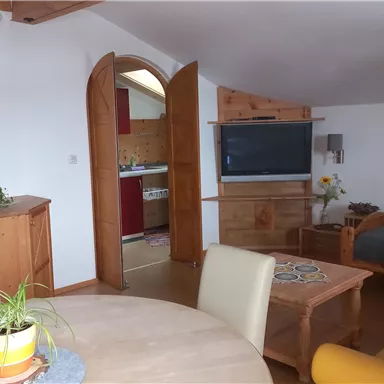 A cozy living corner with a table, chairs, and a sofa. The decor is bright and modern, with an open kitchen in the background.