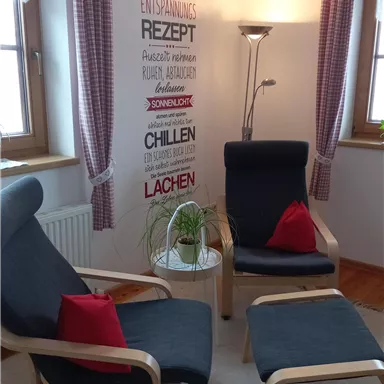 A cozy room with two armchairs and a small table. On the wall, there are decorative words and plants.