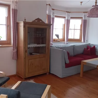 A cozy living space with a gray and red sofa and a wooden coffee table. Large windows let in plenty of light, and a plant on the windowsill adds a natural accent.