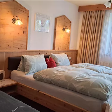Ein gemütliches Schlafzimmer mit zwei Betten aus Holz. Es gibt sanfte Beleuchtung, helle Vorhänge und ein Fenster, das Tageslicht hereinschickt.