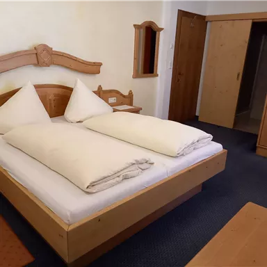 A cozy room with a large double bed and wooden furniture. The walls are painted in light tones, and the room is well lit.