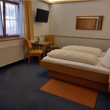 A comfortable hotel room with two beds, a table and chairs. The room has bright curtains and a television on the wall.
