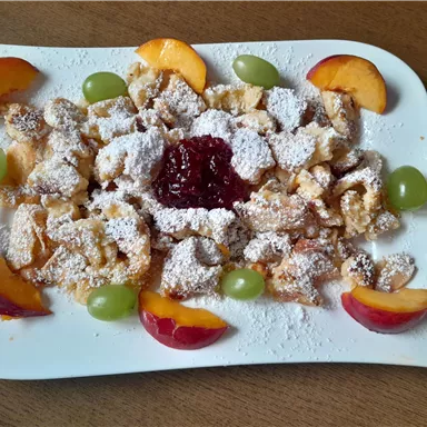 A delicious dessert with baked dough, sprinkled with powdered sugar and served with fruits and jam. The colorful arrangement of peaches and grapes makes the dish appealing.