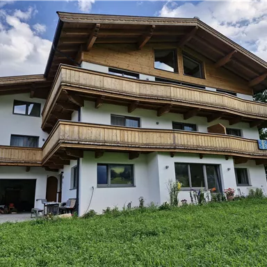 Ein modernes Haus mit mehreren Balkonen und einer schönen Holzfassade. Es befindet sich in einer grünen Umgebung unter einem teilweise bewölkten Himmel.