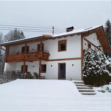 A beautiful house in the snow with wooden elements and a rustic charm. The surroundings are wintry and peaceful.