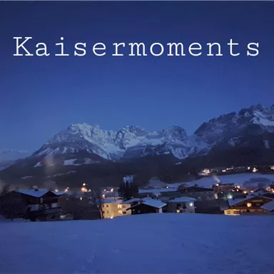 A snow-covered landscape at night with mountains in the background. In the distance, the lights of a small village shine.