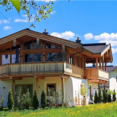 A picturesque building in Alpine style surrounded by green meadows and a clear blue sky. The architecture combines traditional and modern elements.