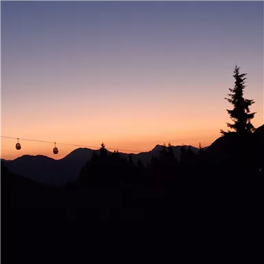 A picturesque sunset over the mountains. Some cable car cabins are floating in the colors of the sky.