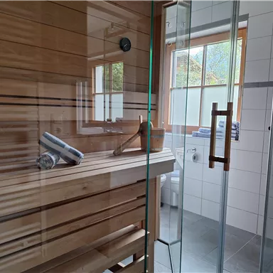 Eine moderne Sauna mit Holzregalen und großer Glasfront. Hell erleuchtet durch Fenster, bietet sie eine entspannende Atmosphäre.