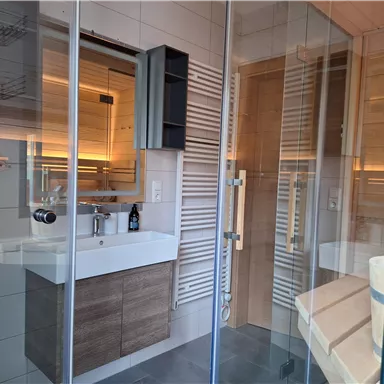 Ein modernes Badezimmer mit einer Glasdusche und einem eleganten Waschtisch. Holzdetails und sanfte Beleuchtung schaffen eine gemütliche Atmosphäre.