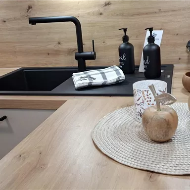 A modern kitchenette with wooden surfaces and minimalist furnishings. On the table, there are decorative items such as a bowl, candles, and a coffee machine.
