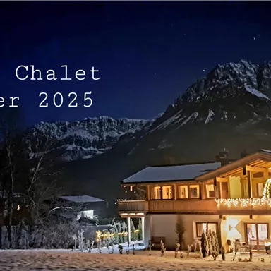 A charming chalet in the snow under a clear night sky. The surroundings are surrounded by majestic mountains, and the chalet is festively illuminated.