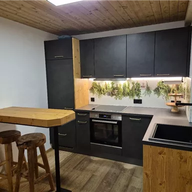 Eine moderne Küche mit dunklen Möbeln und Holzdetails. Im Hintergrund sind Pflanzenmuster an der Wand zu sehen.