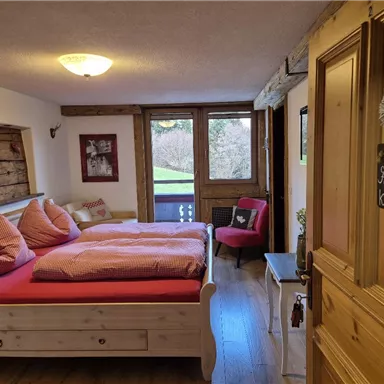 Ein gemütliches Schlafzimmer mit einem großen Bett und roten Kissen. Die Fenster bieten einen Blick auf die grüne Landschaft draußen.