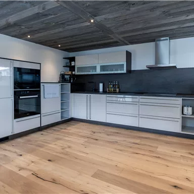 Eine moderne Küche mit weißen Schränken und einem dunklen Arbeitsbereich. Der Boden besteht aus hellem Holz und sorgt für eine einladende Atmosphäre.
