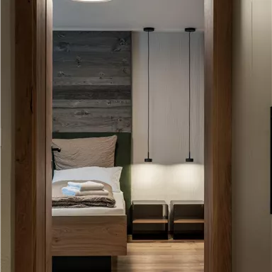 Ein modernes Zimmer mit Holzfußboden und harmonischer Einrichtung. Das Bett ist mit dezenten Farben und kuscheligen Decken dekoriert.
