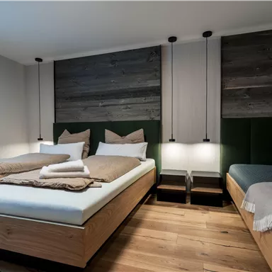 Ein modernes Zimmer mit zwei Betten und Holzfußboden. Die Wände sind in gedeckten Farben gehalten und die Beleuchtung schafft eine gemütliche Atmosphäre.