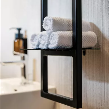 Ein modernes Badezimmer mit einem stilvollen Handtuchhalter. Auf dem Regal liegen gefaltete, weiße Handtücher.