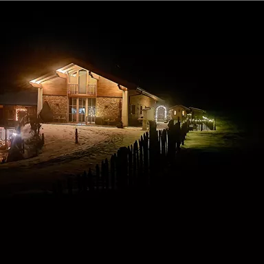 Das Almchalet Riederhäusl in der Nacht, beleuchtet von warmem Licht. Es liegt in einer verschneiten Umgebung mit einer einladenden Atmosphäre.