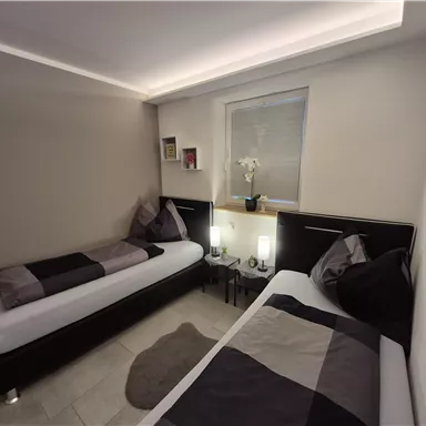 A modern room with two single beds and subtle decorations. The gentle lighting creates an inviting atmosphere.
