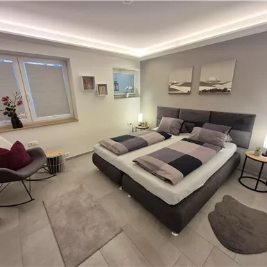 A modern bedroom with a double bed and stylish pillows. Soft lighting and minimalist decoration create an inviting atmosphere.
