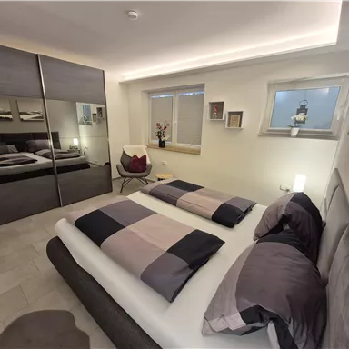 A modern bedroom with two single beds and an elegant wardrobe. The soft lighting and decorative elements give the room a cozy atmosphere.