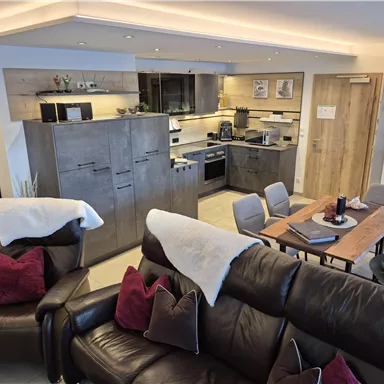 A modern holiday apartment with an open kitchen and a cozy living area. The space is bright and inviting, featuring a dining table and comfortable sofas.