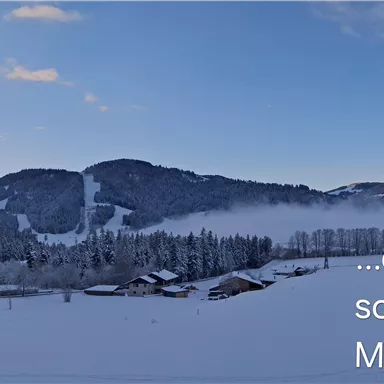 A snow-covered mountain landscape with huts in the foreground. The sky is clear and a gentle morning light is shining.