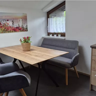 Ein gemütlicher Essbereich mit einem Holztisch und modernen Stühlen. An der Wand hängt ein Bild einer schönen Landschaft mit Blumen.