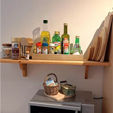 A modern kitchen with a microwave oven and shelves. On the shelves are bottles and cooking utensils.
