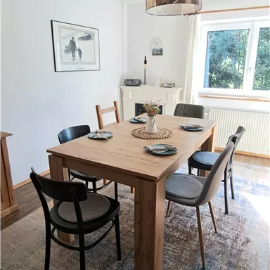 A bright dining area with a wooden table and black chairs. Large windows provide plenty of daylight and a cozy atmosphere.