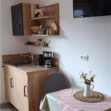 A cozy kitchenette with wooden cabinets and modern amenities. The table is decorated with a tablecloth and a vase.