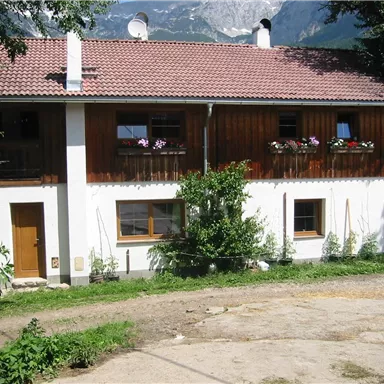 Ein charmantes Haus mit einem roten Satteldach und Holzverkleidung. Vor dem Haus befinden sich Blumen und ein kleiner Garten.