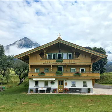 Ein schön gelegenes traditionelles Haus im alpenländischen Stil mit einem großen Balkon. Im Hintergrund ist der imposante Wilde Kaiser zu sehen.