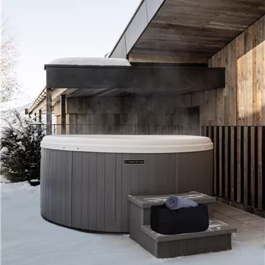 An outdoor hot tub surrounded by snow. The wooden cladding of the house creates a cozy atmosphere.