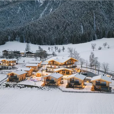 A picturesque winter landscape with snow-covered cottages. The little houses are cozily lit and surrounded by mountains.